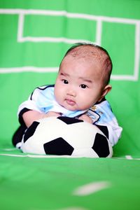 Baby with toy soccer ball on green fabric