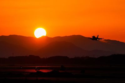Silhouette airplane flying against sky during sunset