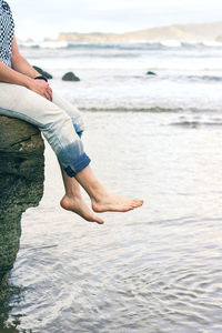 Low section of man sitting on rock over sea