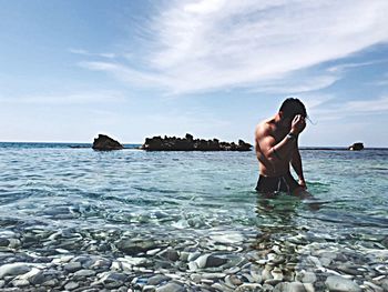 Full length of shirtless man in sea against sky