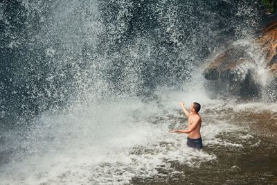 Shirtless man enjoying waterfall in lake
