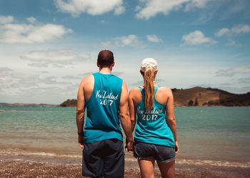 Rear view of couple standing at beach against sky