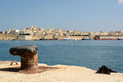 Buildings by sea against clear blue sky