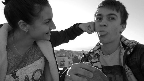 Close-up of playful woman punching man against clear sky