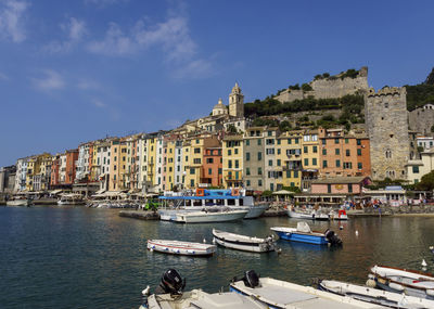 Sailboats moored on sea by buildings in city against sky