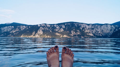 Low section of person legs in lake against mountains