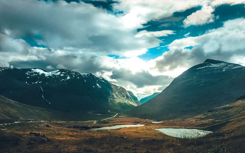 Scenic view of landscape by mountains against cloudy sky