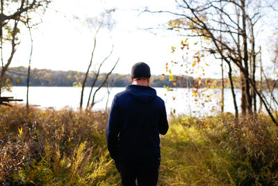 Rear view of man standing on field by lake against sky