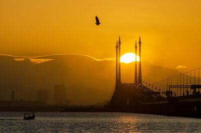 Silhouette bridge over river against sky during sunset