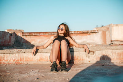 Full length of young woman sitting against sky