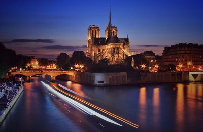 Light trails on river amidst buildings at dusk