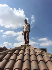 Low angle view of man standing on roof against sky