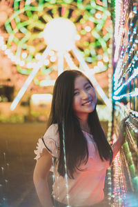 Digital composite portrait of smiling young woman standing at amusement park during night