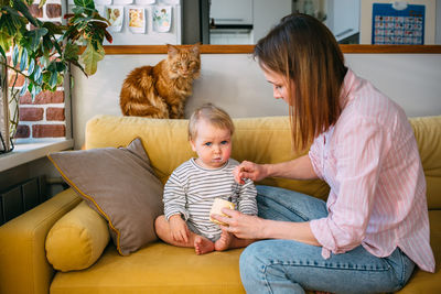 Side view of mother and daughter sitting on sofa at home