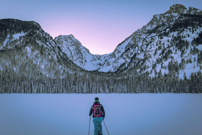 Rear view of woman with ski poles standing against snow covered mountains