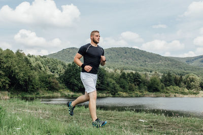 Full length of young man jogging on grassy field by lake