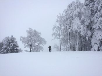 Man walking on snow covered field against sky