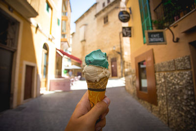 Woman holding ice cream cone against buildings in city