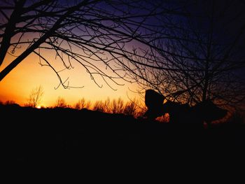 Silhouette man sitting on field against sky at sunset