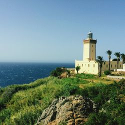 Lighthouse by sea against clear sky