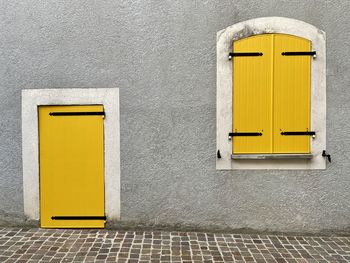 Closed yellow door and wooden shutters on the facade of the grey house 