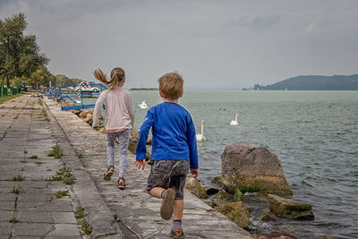Rear view of children running on promenade by river