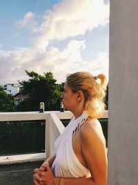 Side view of young woman standing against sky