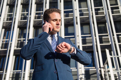 Low angle view of businessman talking on smart phone while standing against building