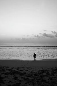 Rear view of silhouette man walking on beach against sky