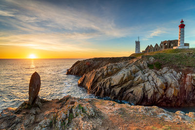 Lighthouse by sea against sky during sunset