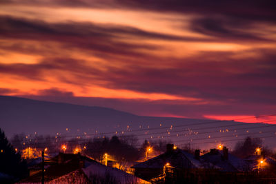 Illuminated cityscape against dramatic sky at sunset