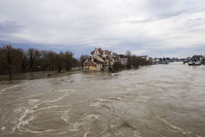 Buildings by river against cloudy sky