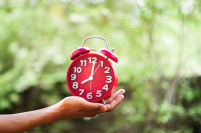 Close-up of hand holding alarm clock against blurred background