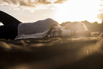 Portrait of woman lying down on sand against sky