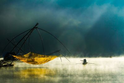 People in boat on lake by fishing net during foggy weather