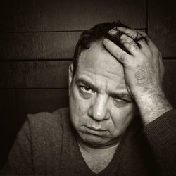 Close-up portrait of sad mature man with head in hand by wall