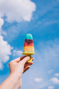 Cropped hand holding ice cream cone against sky