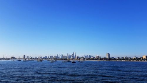Sea by modern buildings against clear blue sky