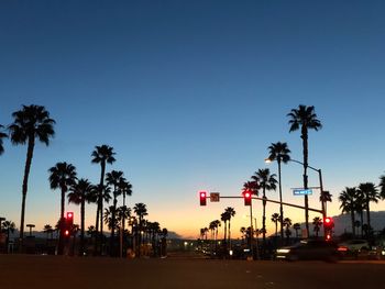 Silhouette palm trees by road against sky during sunset