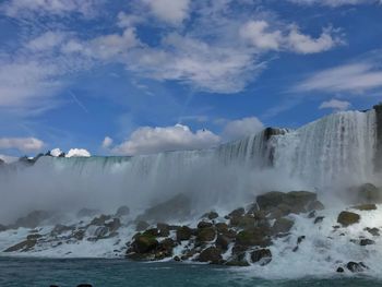 Scenic view of waterfall against cloudy sky