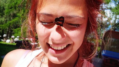 Close-up of smiling young woman with butterfly on sunny day