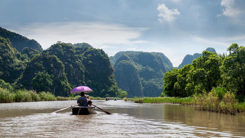 People rowing boat in river against sky