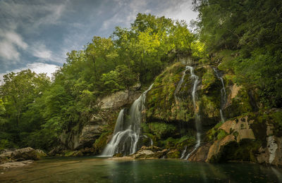 Scenic view of waterfall in forest against sky