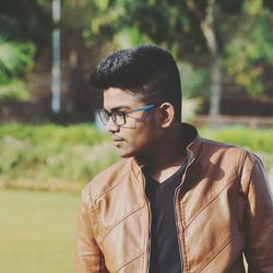 Young man looking down while wearing jacket and eyeglasses