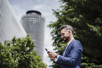 Young man using mobile phone against trees