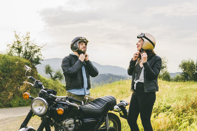 Couple wearing helmets while standing by motorcycle against sky