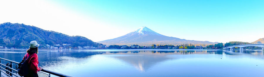 Woman standing by railing over lake against clear sky