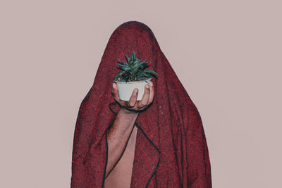 Scarf covered man holding potted plant against beige background