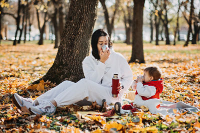 Happy family mother and little toddler baby daughter having autumn picnic with red thermos and cup