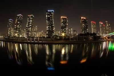 Illuminated buildings by river against sky at night